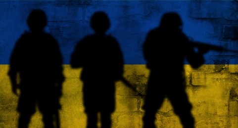 Silhouettes of soldiers and wall painted in Ukrainian flag colors on background. Military service during war