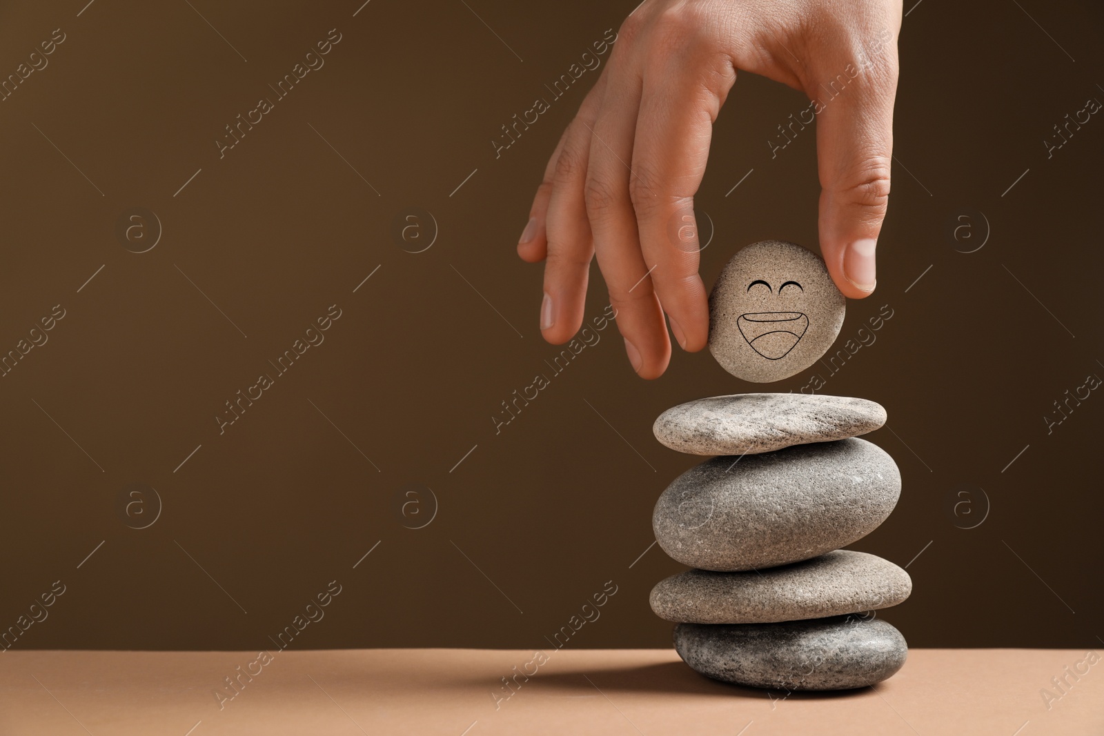 Photo of Closeup view of woman putting stone with drawn happy face on stack against dark beige background, space for text. Zen concept