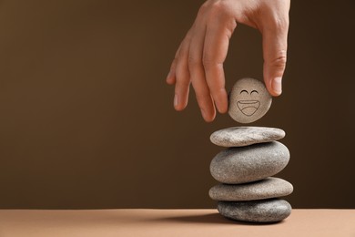 Photo of Closeup view of woman putting stone with drawn happy face on stack against dark beige background, space for text. Zen concept
