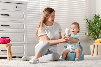 Photo of Mother training her child to sit on baby potty indoors