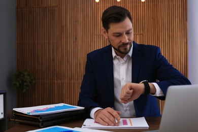 Photo of Businessman looking at wristwatch while working with documents in office