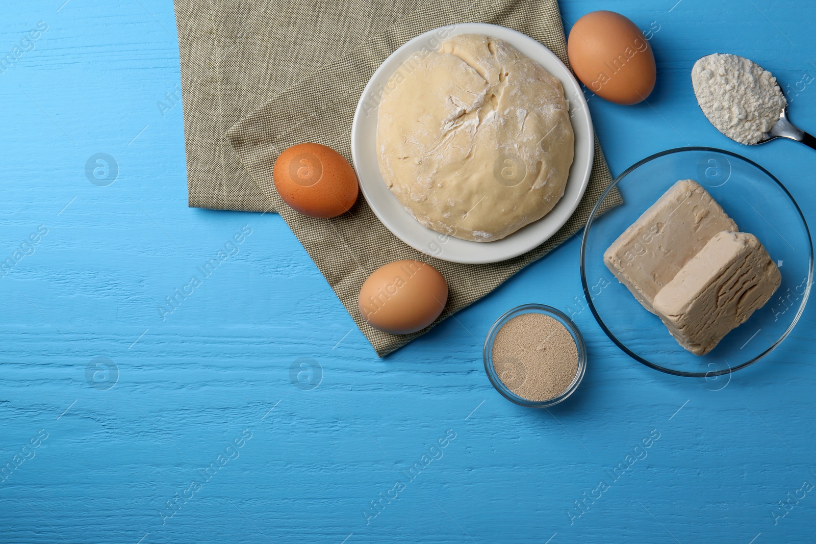 Photo of Different types of yeast, eggs, dough and flour on light blue wooden table, flat lay. Space for text