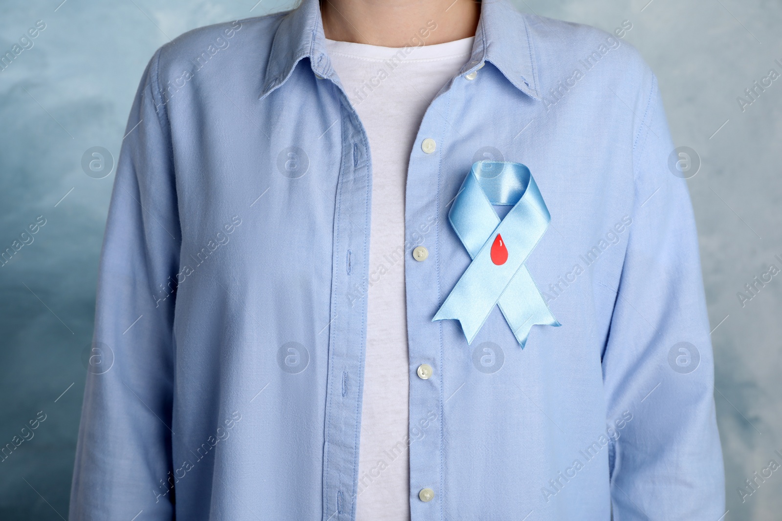 Photo of Woman with light blue ribbon and paper blood drop on color background, closeup. World Diabetes Day