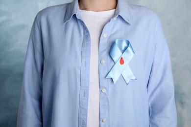 Woman with light blue ribbon and paper blood drop on color background, closeup. World Diabetes Day