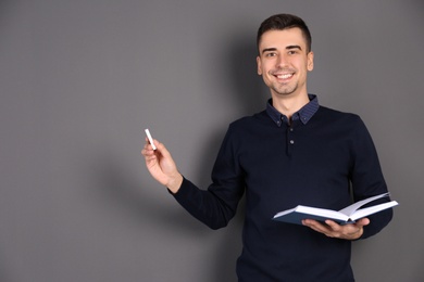 Photo of Young male teacher with chalk and book on grey background