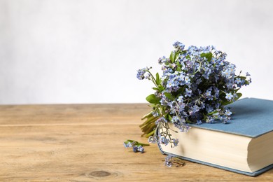 Bouquet of beautiful forget-me-not flowers and book on wooden table against light background, space for text
