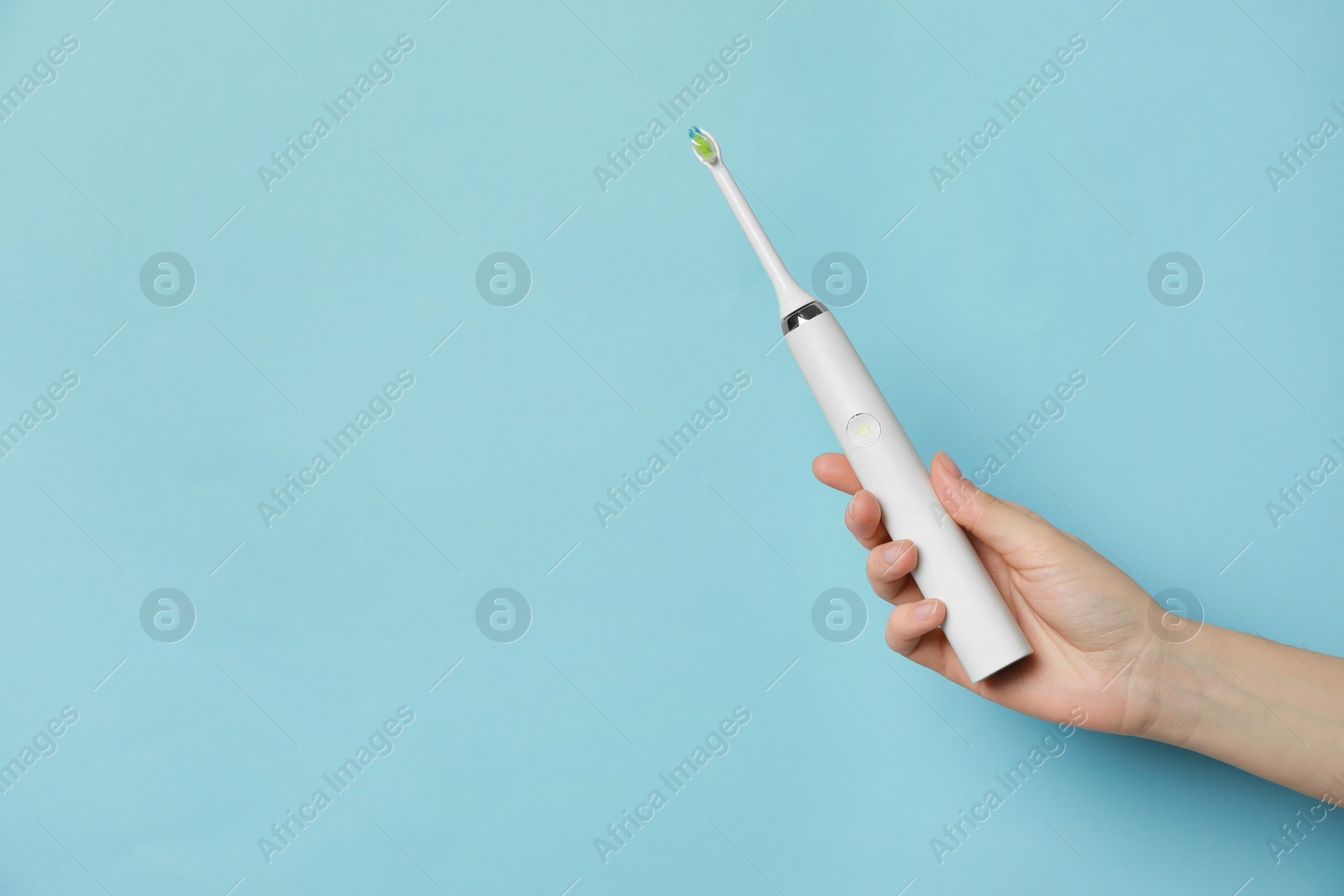 Photo of Woman holding electric toothbrush on light blue background, closeup. Space for text