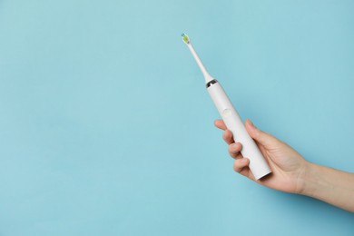 Photo of Woman holding electric toothbrush on light blue background, closeup. Space for text