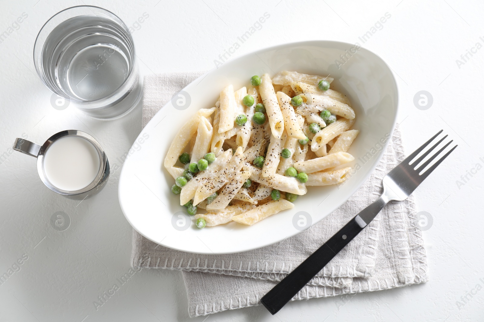 Photo of Delicious pasta with green peas, creamy sauce, water and fork on white table, top view