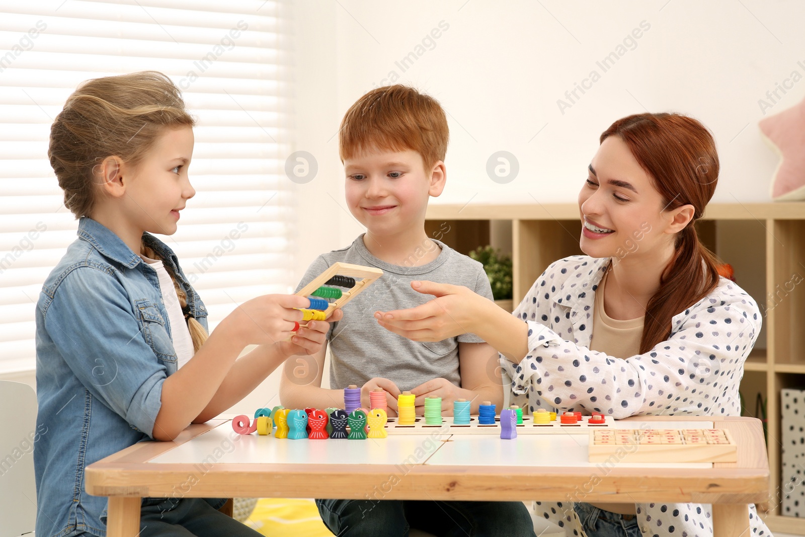 Photo of Happy mother and children playing with different math game kits at desk in room. Study mathematics with pleasure