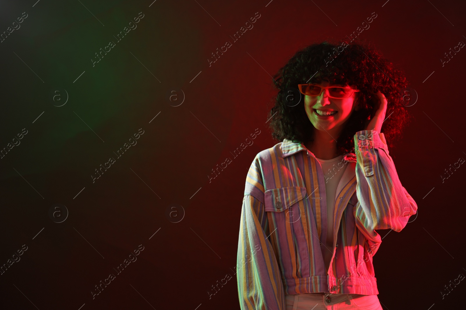 Photo of Beautiful young woman in sunglasses posing on color background in neon lights. Space for text