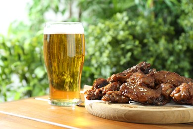 Photo of Tasty roasted chicken wings and glass of beer on wooden table, closeup