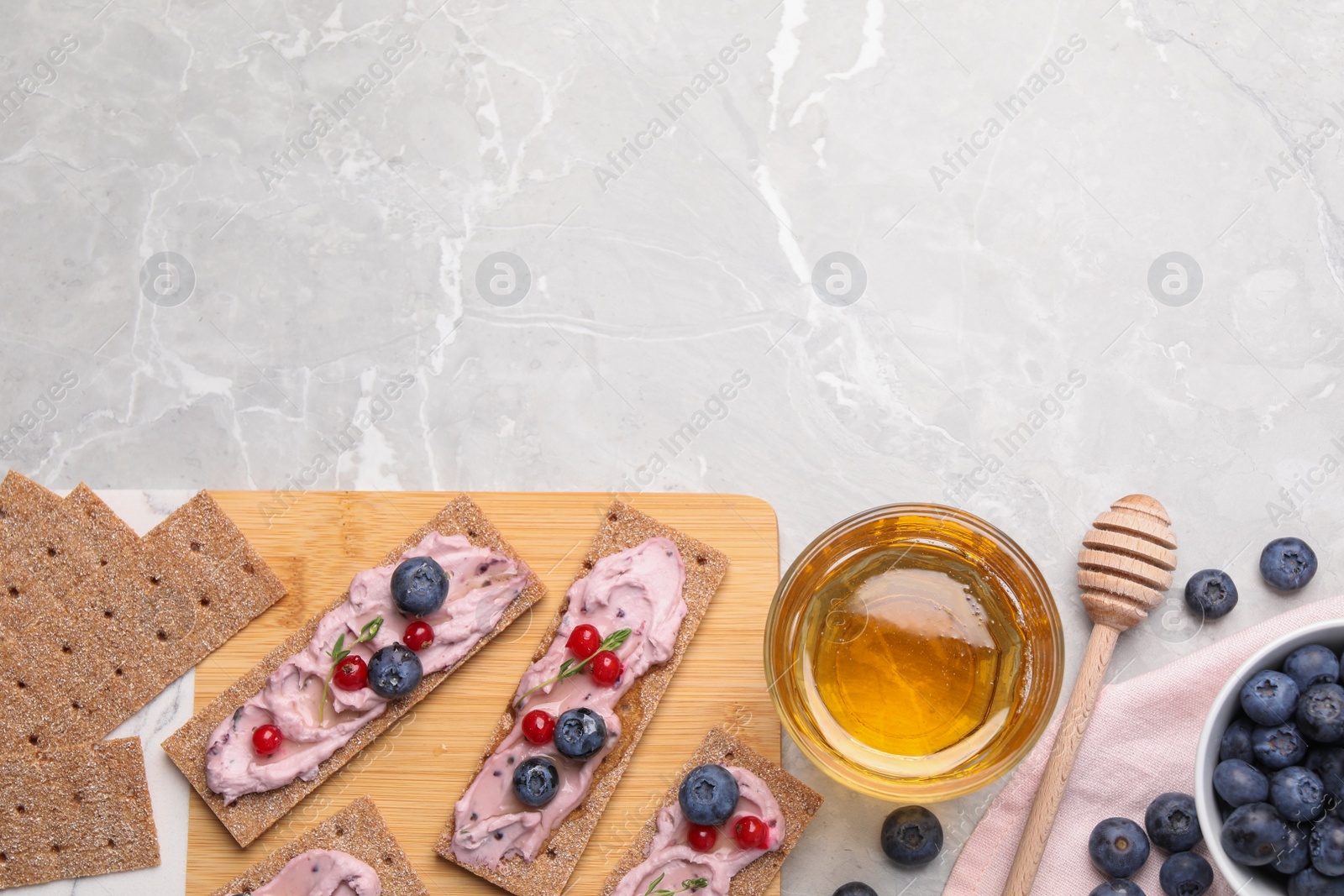 Photo of Tasty cracker sandwiches with cream cheese, blueberries, red currants, thyme and honey on light grey marble table, flat lay. Space for text