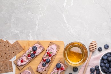 Photo of Tasty cracker sandwiches with cream cheese, blueberries, red currants, thyme and honey on light grey marble table, flat lay. Space for text