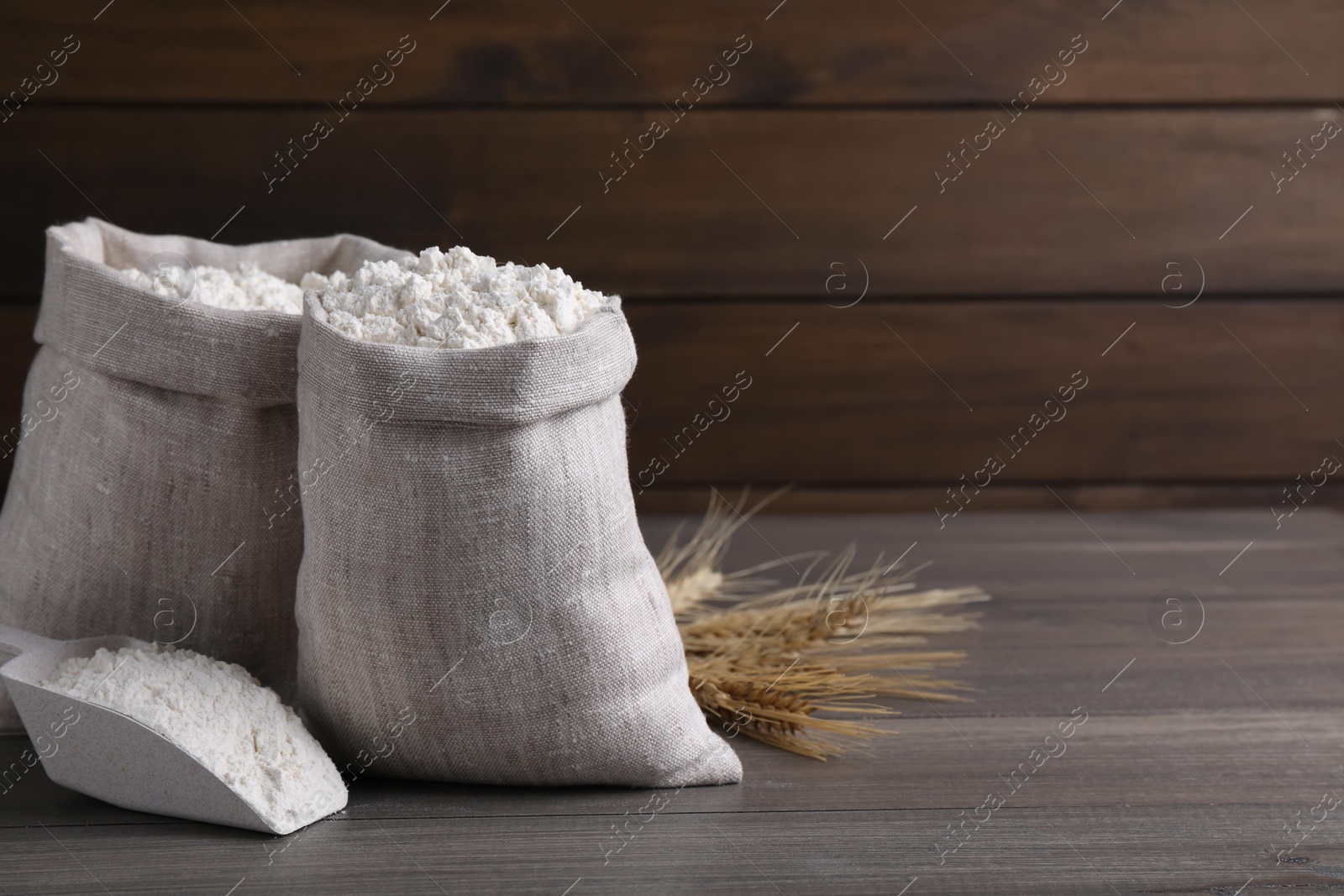 Photo of Sacks with flour and wheat spikes on wooden background. Space for text