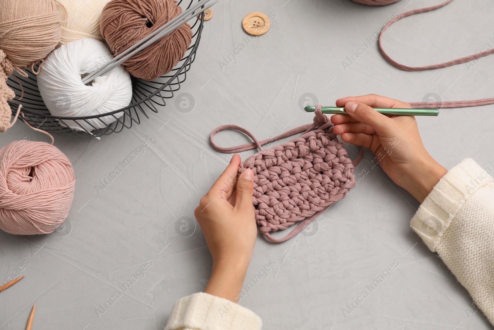 Photo of Woman crocheting with threads at grey table, closeup. Engaging hobby