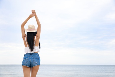 Photo of Beautiful young woman with beach hat near sea, back view. Space for text