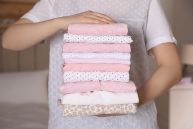 Photo of Woman holding stack of girl's clothes in bedroom, closeup