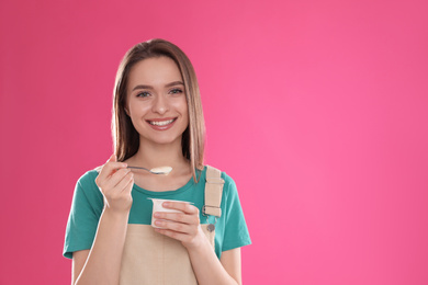 Young attractive woman with tasty yogurt on pink background. Space for text