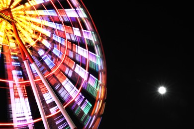 Photo of Beautiful glowing Ferris wheel against dark sky, low angle view. Space for text