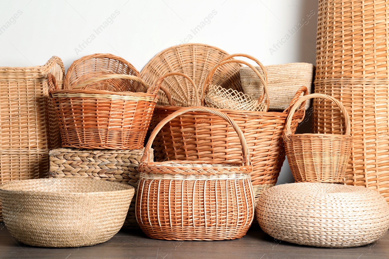 Photo of Many different wicker baskets made of natural material on floor near light wall