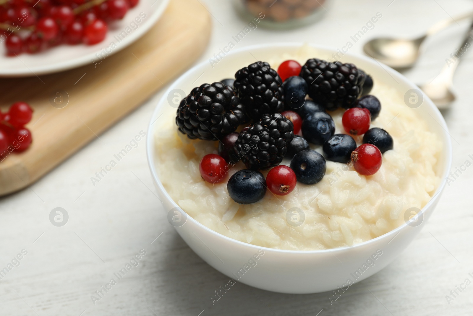 Photo of Delicious rice pudding with berries on white wooden table, closeup