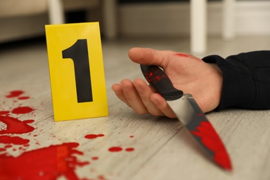 Photo of Crime scene marker and dead body with bloody knife on floor, closeup