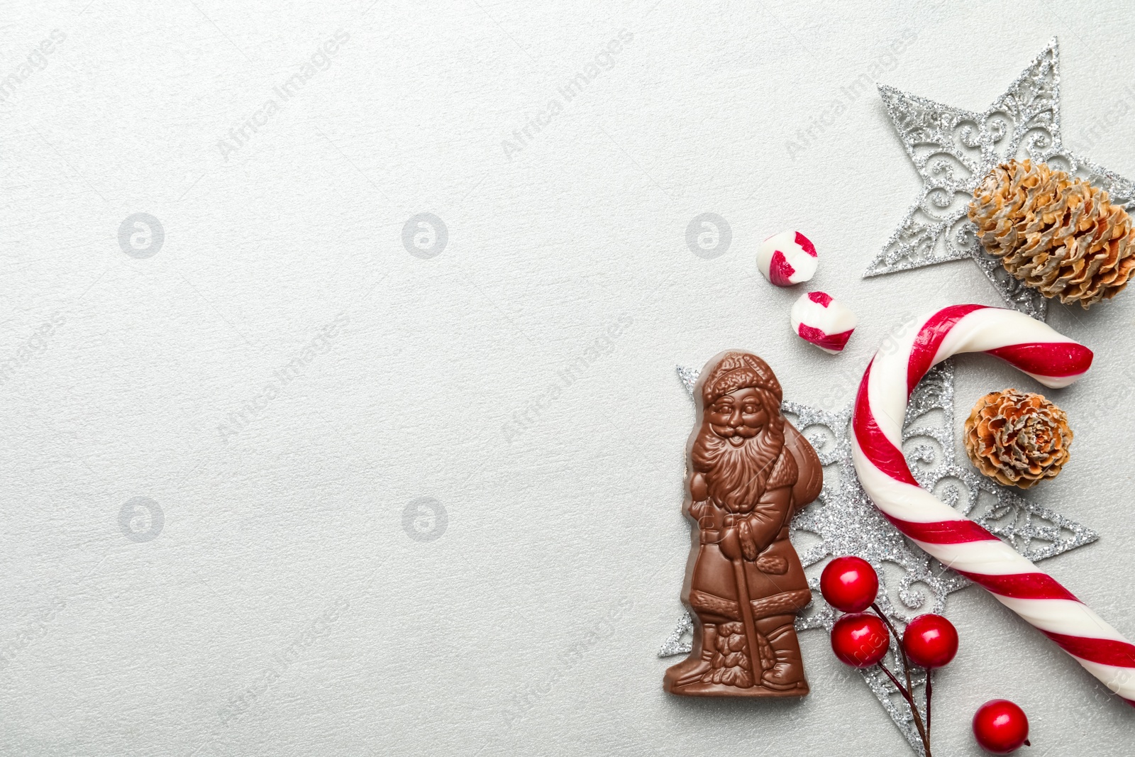 Photo of Flat lay composition with chocolate Santa Claus, candy cane and Christmas decorations on light grey background. Space for text