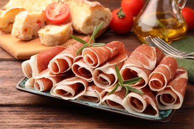 Photo of Rolled slices of delicious jamon with rosemary on wooden table