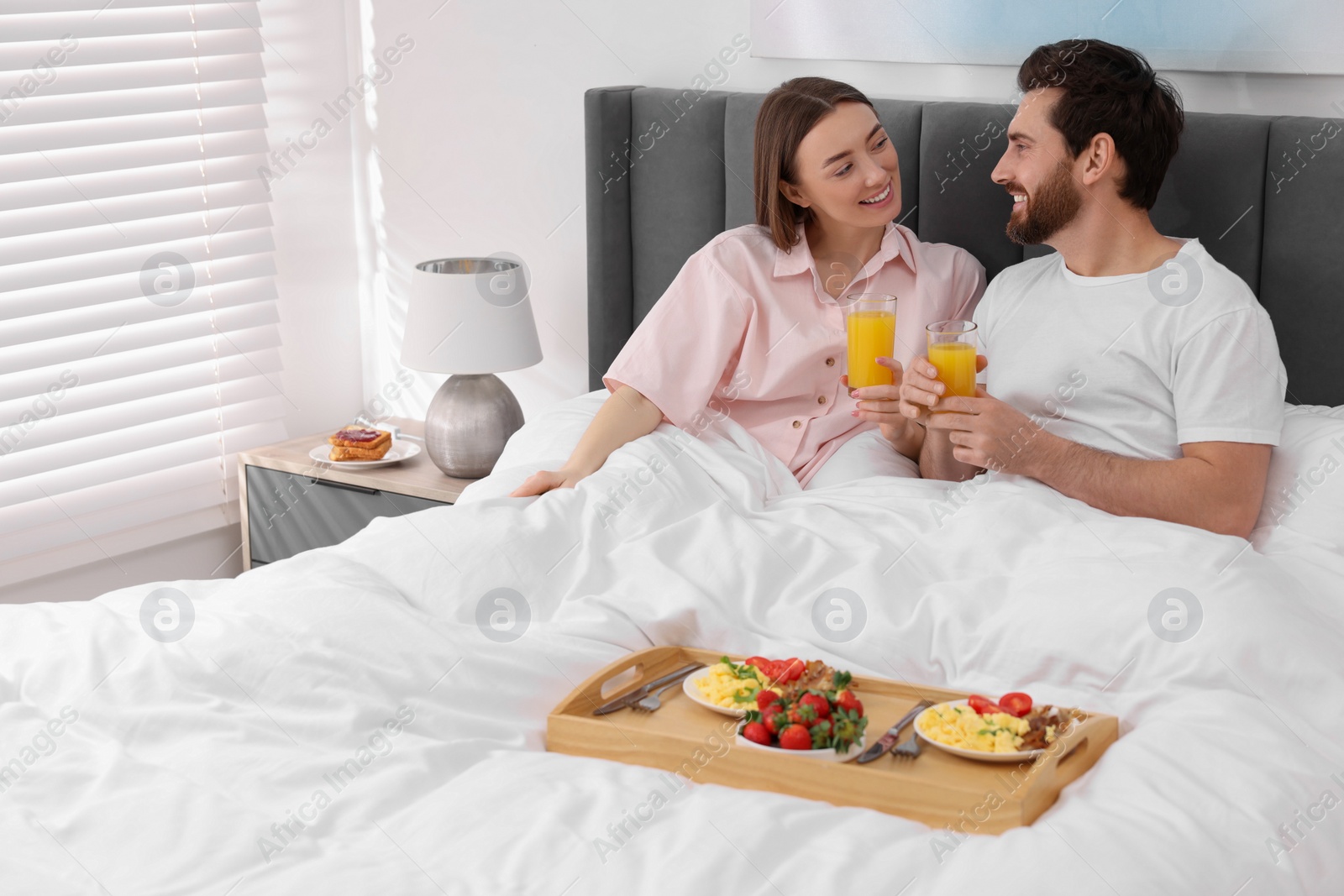 Photo of Happy couple eating tasty breakfast in bed at home. Space for text