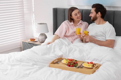 Photo of Happy couple eating tasty breakfast in bed at home. Space for text