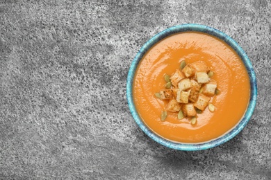 Photo of Tasty creamy pumpkin soup with croutons and seeds in bowl on grey table, top view. Space for text