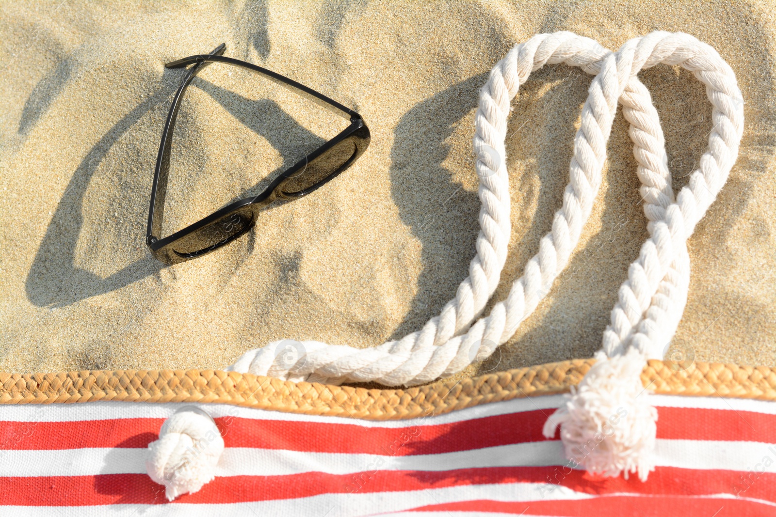 Photo of Stylish sunglasses and beach bag on sand, flat lay