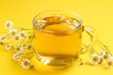 Cup of tea and chamomile flowers on yellow background