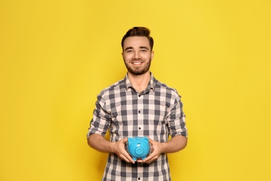 Young man with piggy bank on color background