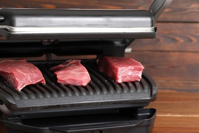 Photo of Electric grill with raw meat on table, closeup