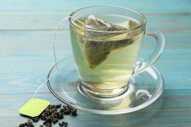 Tea bag in cup with hot drink and dry leaves on light blue wooden table, closeup