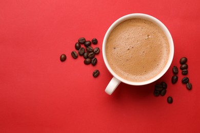 Photo of Fresh coffee in cup and roasted beans on red background, top view. Space for text