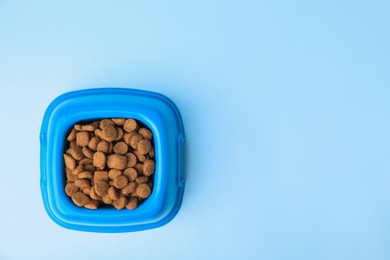 Photo of Dry pet food in feeding bowl on light blue background, top view. Space for text