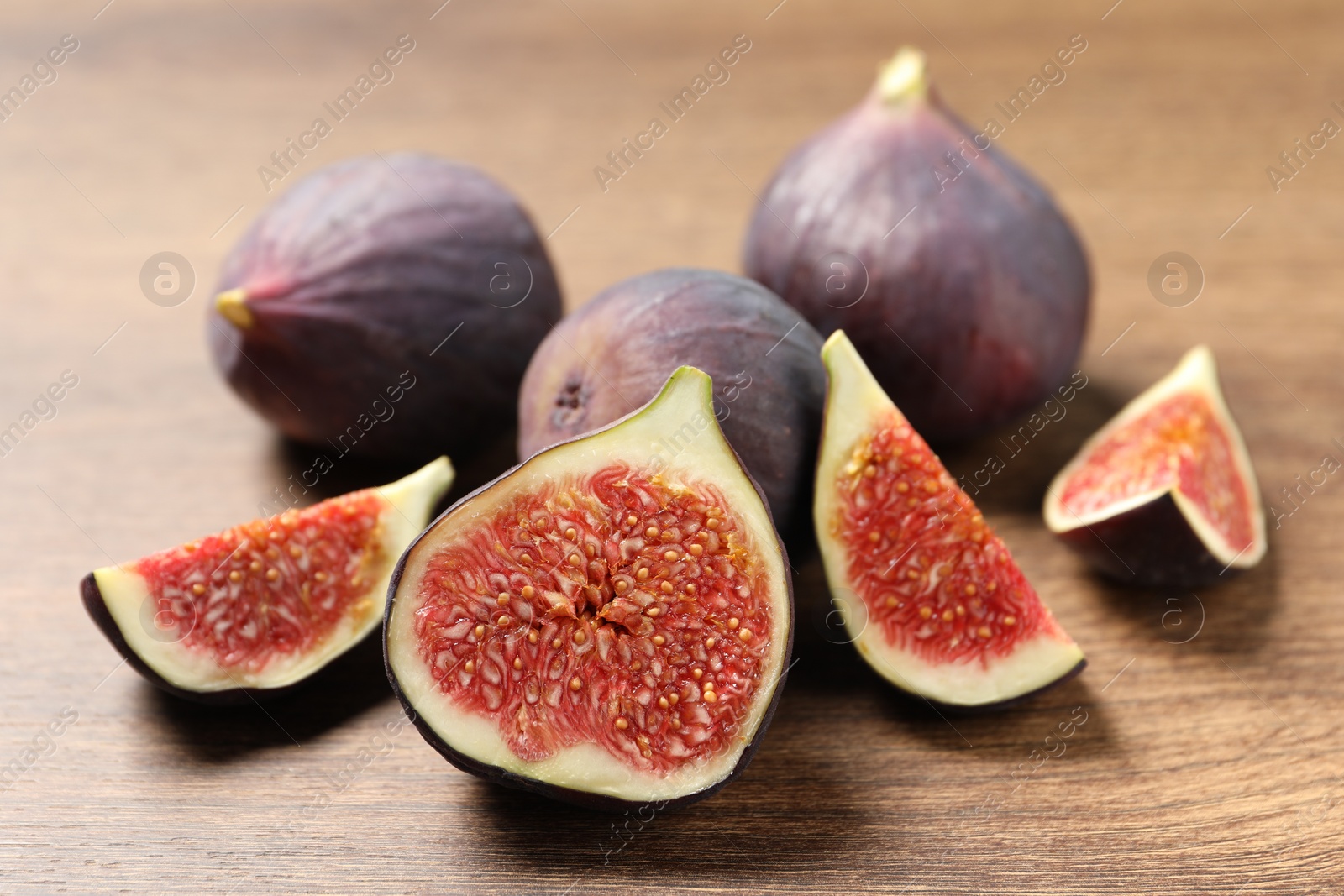 Photo of Whole and cut ripe figs on wooden table, closeup