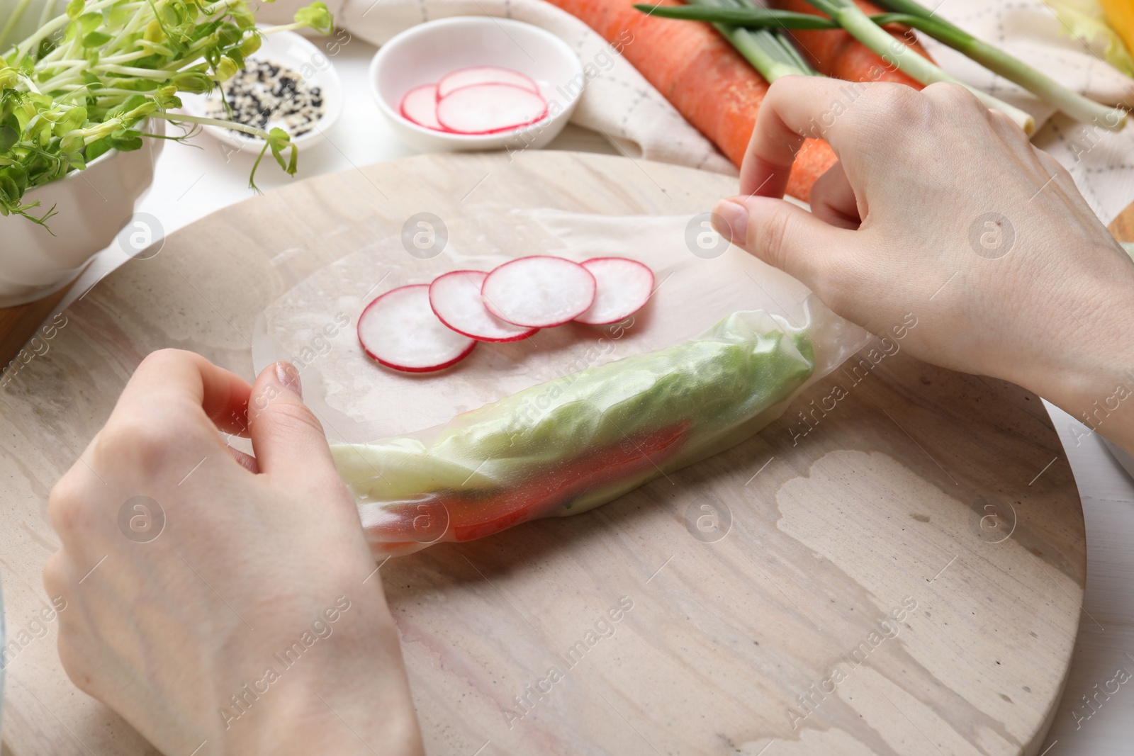 Photo of Woman wrapping spring roll at table with products, closeup