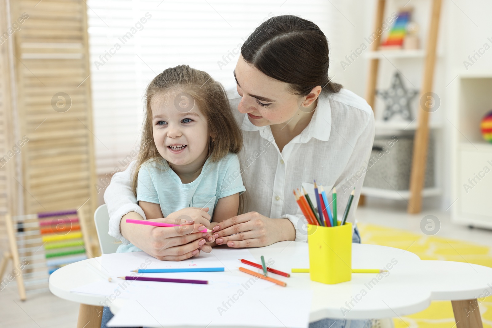 Photo of Mother and her little daughter drawing with colorful pencils at home