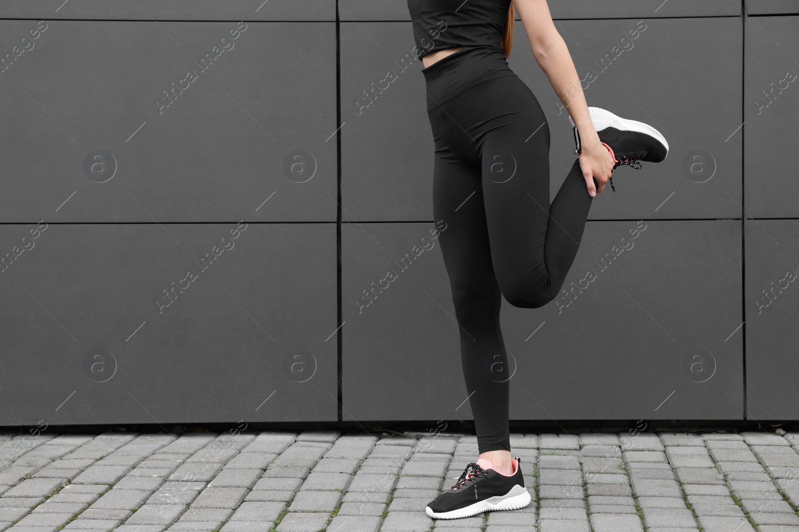 Photo of Woman in gym clothes doing exercises near grey wall on street, closeup. Space for text