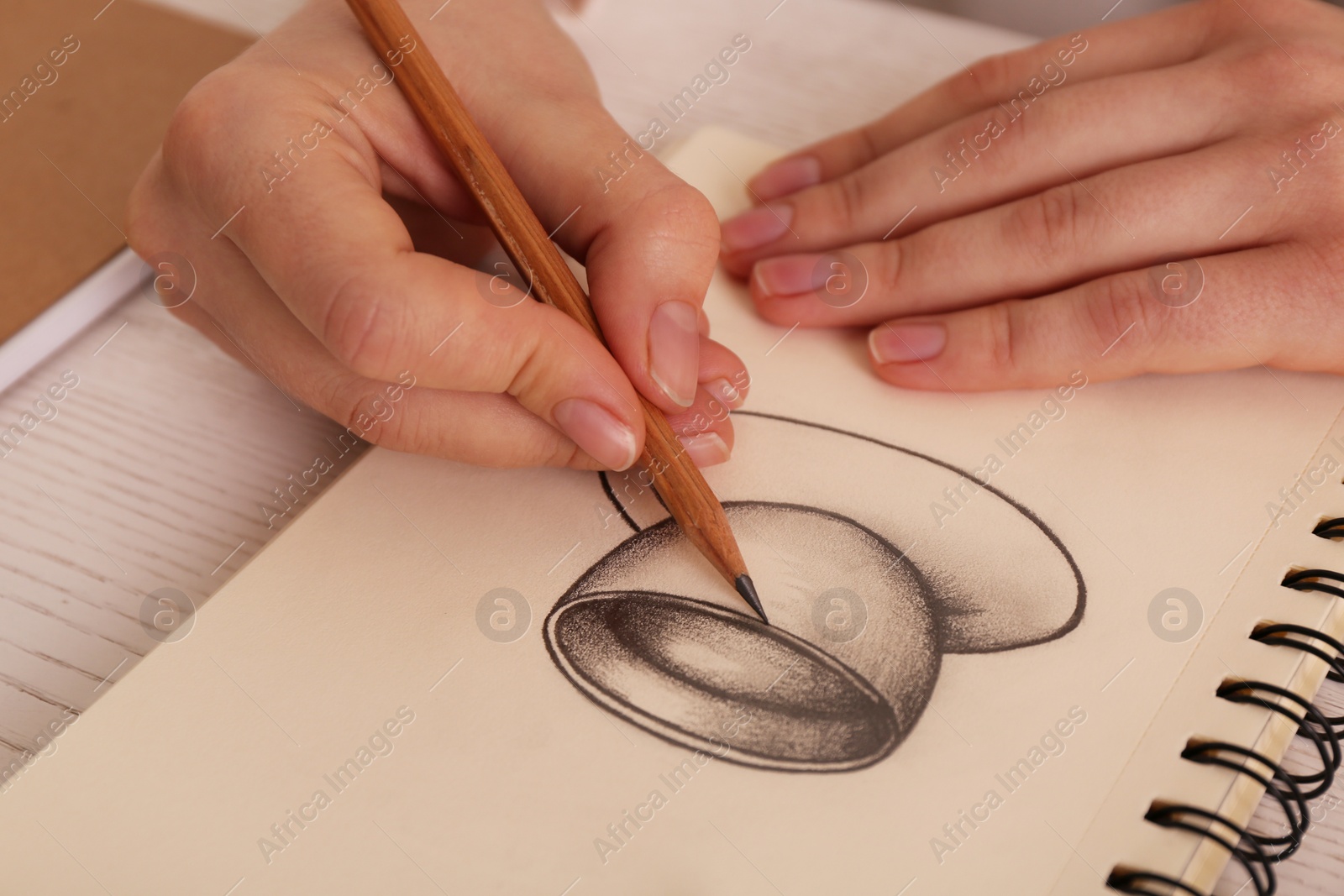 Photo of Woman drawing cup of drink with graphite pencil in sketchbook at table, closeup