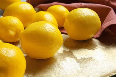 Photo of Ripe whole lemons on golden plate, closeup