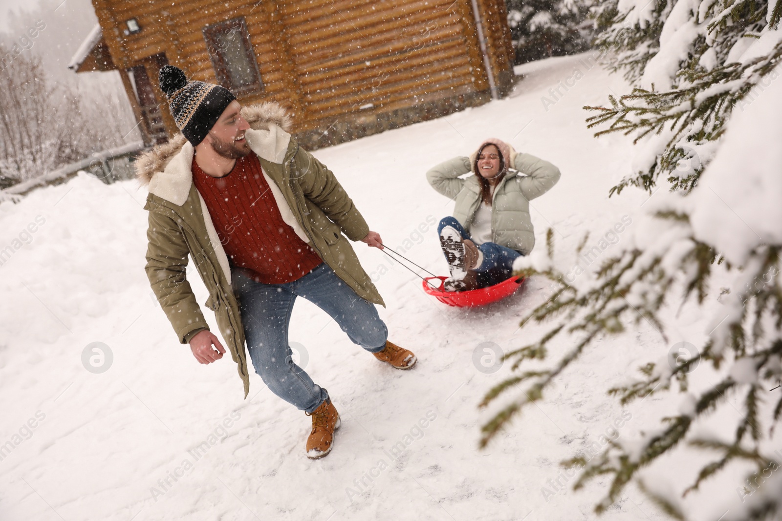 Photo of Young man pulling sled with his girlfriend outdoors on snowy day. Winter vacation