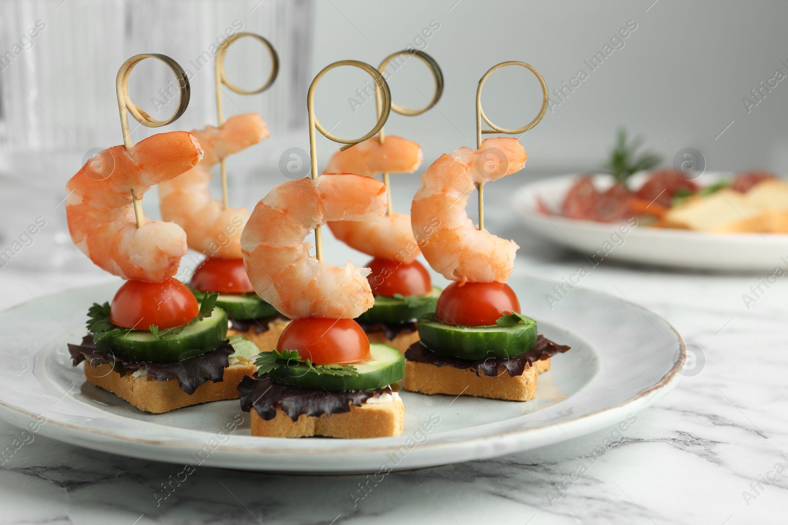 Photo of Tasty canapes with shrimps, cucumber, greens and tomatoes on white marble table, closeup