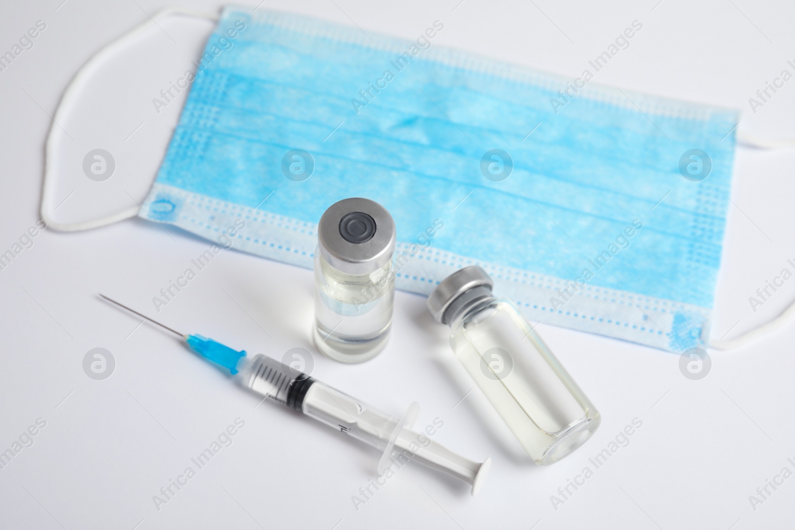 Photo of Vials, syringe and surgical mask on light background. Vaccination and immunization