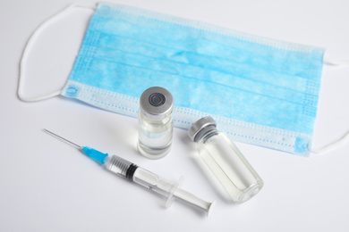 Vials, syringe and surgical mask on light background. Vaccination and immunization