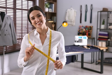 Photo of Happy dressmaker with measuring tape in workshop, space for text